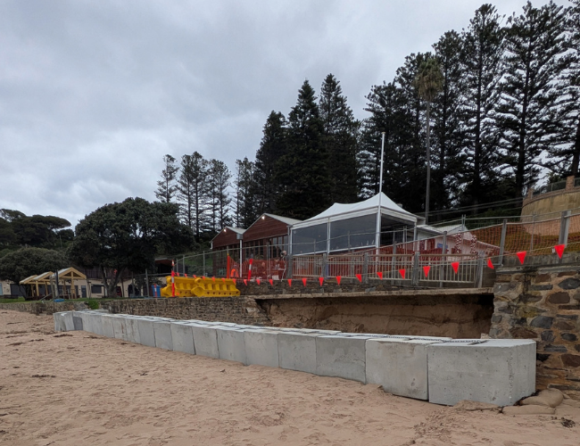 View of beach at Horseshoe Bay with concrete blocks acting as a temporary barrier in front of collapsed seawall.