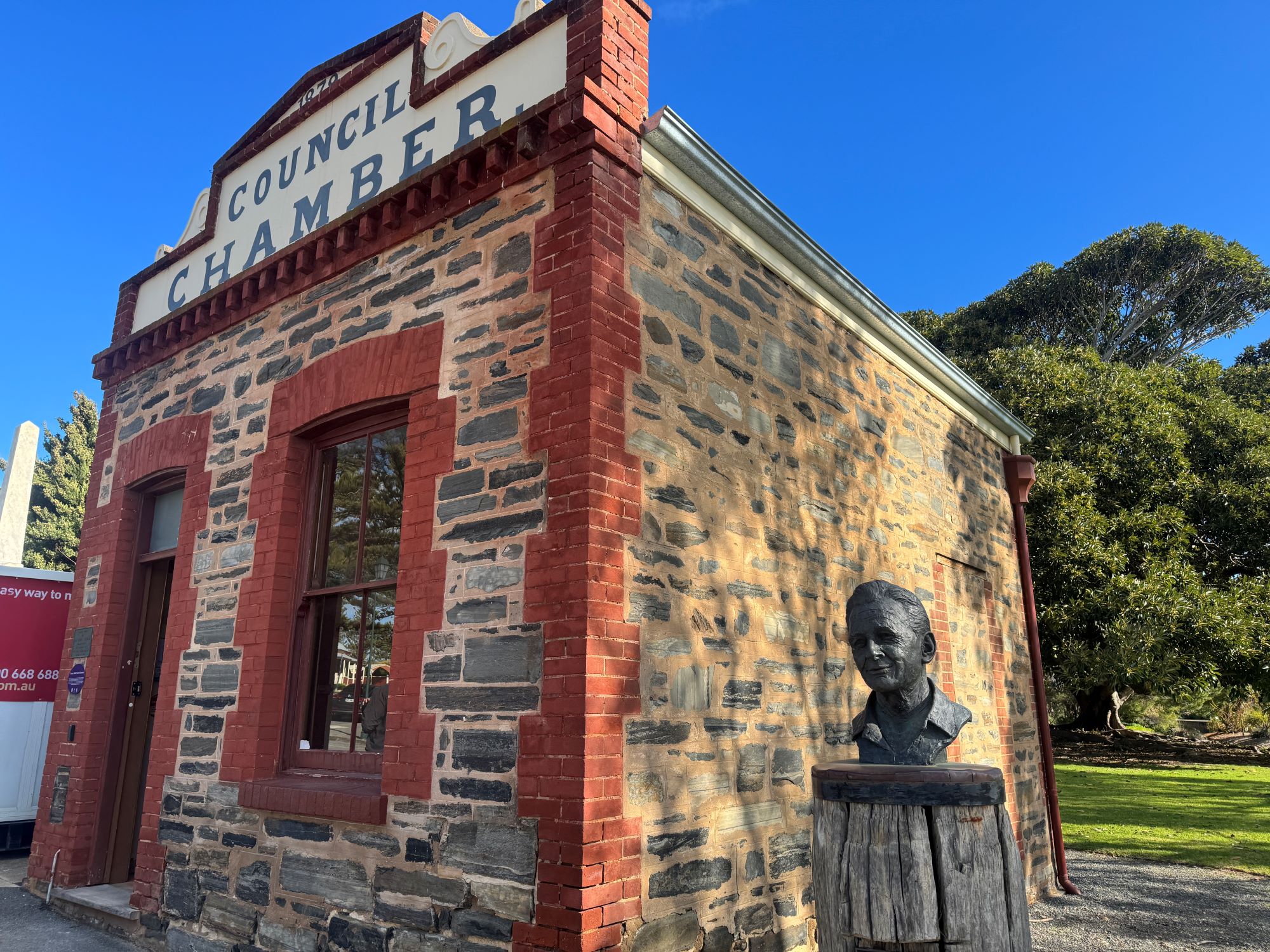 External view of heritage listed Port Elliot Council Chamber made from local stone with Council Chamber sign above the door and a bronze bust of local identity Joe Barton on timber plinth.