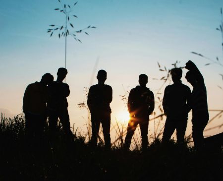six men in nature. They are in silhouette and are facing the setting sun    