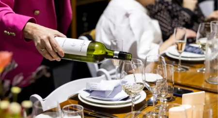 Waiter in pink jacket pours Bremerton white wine into glass placed on formally set table in cellar door.